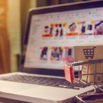Image of laptop on desk next to miniature shopping cart